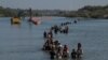 Una caravana pasa junto a una serie de boyas, que se construyen para disuadir a los migrantes de cruzar el río Grande, mientras buscan una abertura en el alambre de concertina para ingresar a Eagle Pass, Texas, EEUU, el 27 de julio de 2023.