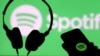 Unos auriculares y un teléfono inteligente frente a una pantalla con el logotipo de Spotify. [Foto de archivo]