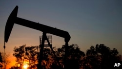 ARCHIVO - El sol se pone detrás de un pozo de petróleo en un campo cerca de El Tigre, Venezuela, en febrero de 2015.