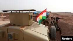 A Kurdish flag is seen next to Peshmerga fighters taking position with their weapons on the frontline against the Islamic State, on the outskirts of Mosul, Iraq, Jan. 26, 2015.