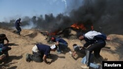 Para pengunjuk rasa Palestina berlindung dari tembakan senjata api pasukan Israel selama unjuk rasa menandai Hari Al-Quds, di perbatasan Israel-Gaza di bagian selatan Jalur Gaza, 8 Juni 2018 (foto: REUTERS/Ibraheem Abu Mustafa)