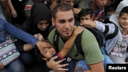 Seorang pria menggendong seorang bocah saat pengungsi dan migran menanti untuk menyeberang perbatasan Yunani dan Makedonia, dekat desa Idomeni (6/9). 