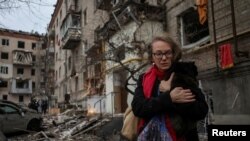 Seorang warga lokal tampak menggendong seekor kucing dan pergi meninggalkan gedung apartemen yang hancur akibat serangan misil Rusia, di Kharkiv, pada 2 Januari 2024. (Foto: Reuters/Sofiia Gatilova)