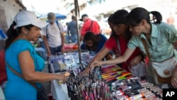 School teacher Daixy Aguero, left, sells makeup at a market in Caracas, Oct. 5, 2019. Aguero holds her chin up when students wander by surprised to spot their teacher selling makeup on weekends at a Caracas market.