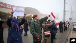 Pengunjuk rasa mengacungkan bendera Belarus yang lama dan poster bertuliskan "(Lukashenko) Pergi" dalam demo menentang hasil pilpres, di Minsk, Belarus, 4 Januari 2021. (Foto: AP)