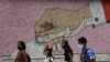 Jóvenes con mascarillas pasan frente a un mural de mosaico con la imagen de una mano depositando una boleta, en Caracas, Venezuela, el domingo. Octubre 11, de 2020.