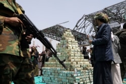 FILE - Houthi followers stand by bills of Yemeni currency during a ceremony held by Houthis to collect supplies for their fighters battling government forces in various front lines, in Sanaa, Yemen, Sept. 24, 2020.