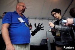 A journalist takes notes while talking with Johnny Matheny (L), from the Johns Hopkins University Applied Physics Lab, as he shows his prosthetic hand during the DARPA (Defense Advanced Research Projects Agency) Demo Day exhibition at the Pentagon.