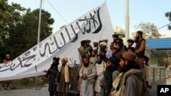 Taliban fighters pose for a photo while raising their flag at Ghazni provincial governor's house, in Ghazni, southeastern Afghanistan, Aug. 15, 2021. 