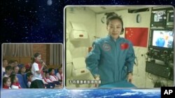 Dalam gambar yang diambil dari kamera CCTV, astronot perempuan China, Wang Yaping (nampak pada layar) sedang mendengarkan pertanyaan dari seorang pelajar putri di Beijing, China, dalam siaran langsung yang dipancarkan dari pesawat antariksa Tiangong-1 (20/6).