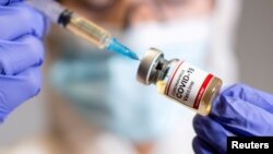 Seorang perempuan memegang botol kecil berlabel stiker "Vaksin Virus Corona" dan jarum suntik medis dalam ilustrasi yang diambil pada 19 Oktober 2020. (Foto: Reuters)